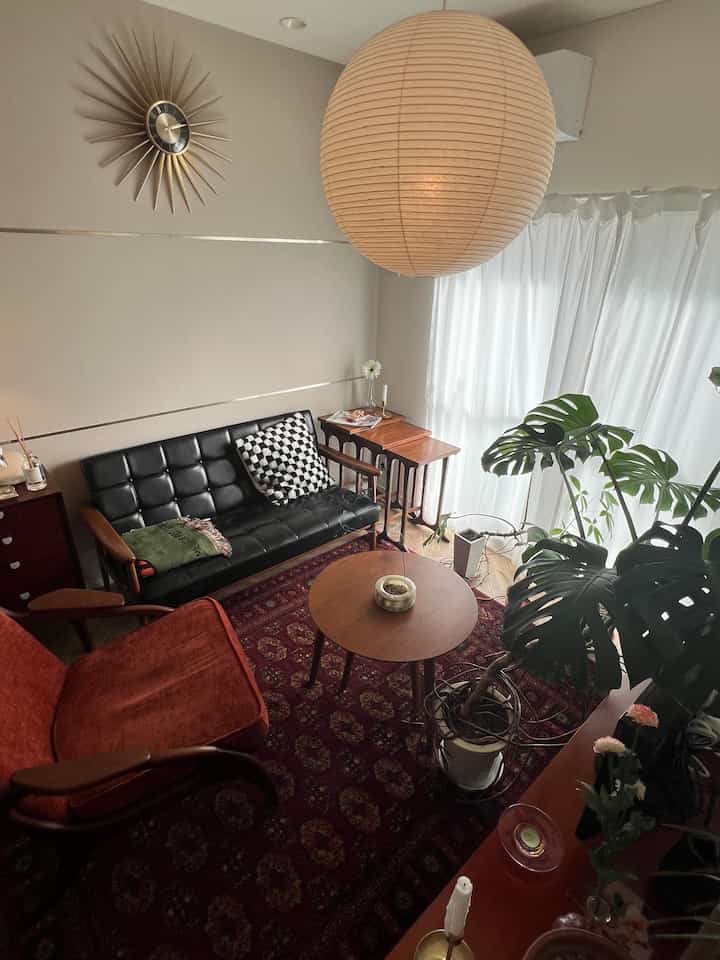 白いカーテンと茶色の木製家具が配置されたミッドセンチュリーモダンのリビング、観葉植物が温かみのある雰囲気を演出