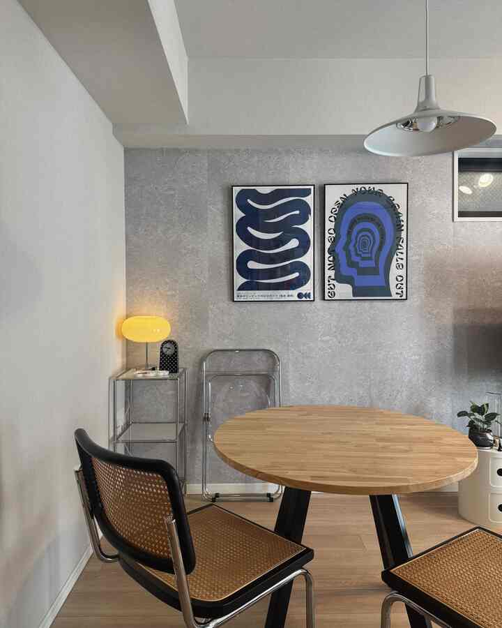 ナチュラルなホワイトとグレーの色調のダイニング、丸い無垢材テーブルとメッシュチェアが配置されたミニマルな印象的な空間