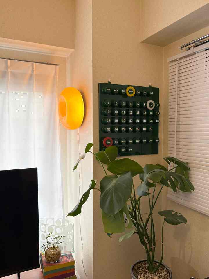 ナチュラルトーンの12畳1LDKリビング、大きな植物とオレンジの壁照明、ブラインドが配置された雰囲気のある空間