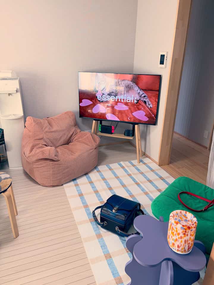 ライトブラウンの床と壁にピンクのビーズクッションやテレビ、ソファが配置された居心地の良いリビング