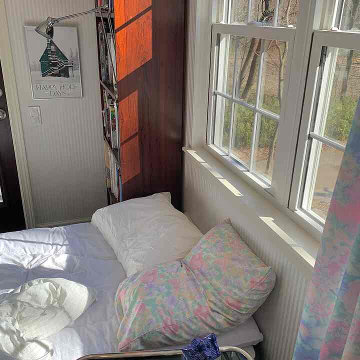 明るいホワイトと木目調が調和した正方形の寝室、窓際に配置されたベッドとポスターが落ち着いた雰囲気を演出