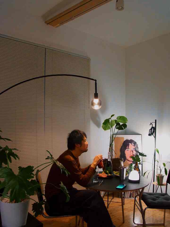 ライトグレーの壁とブラックの丸テーブルが置かれたリビング、植物とフロアランプが配置されたシンプルでナチュラルなインテリア