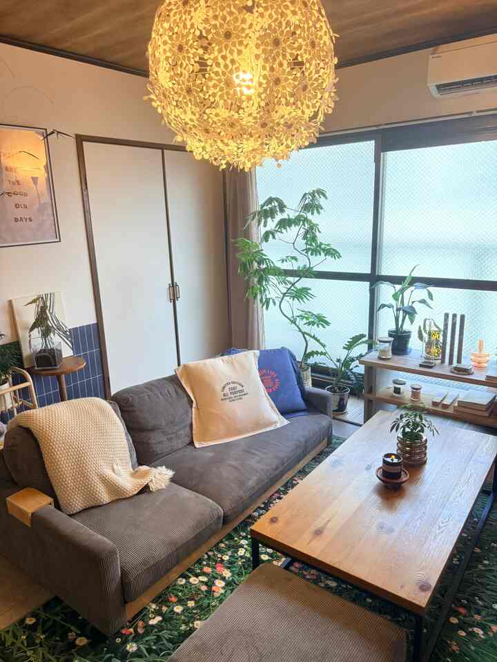 Natural toned living room featuring brown sofa, floral-patterned rug, large plants, and wooden coffee table in a cozy setting