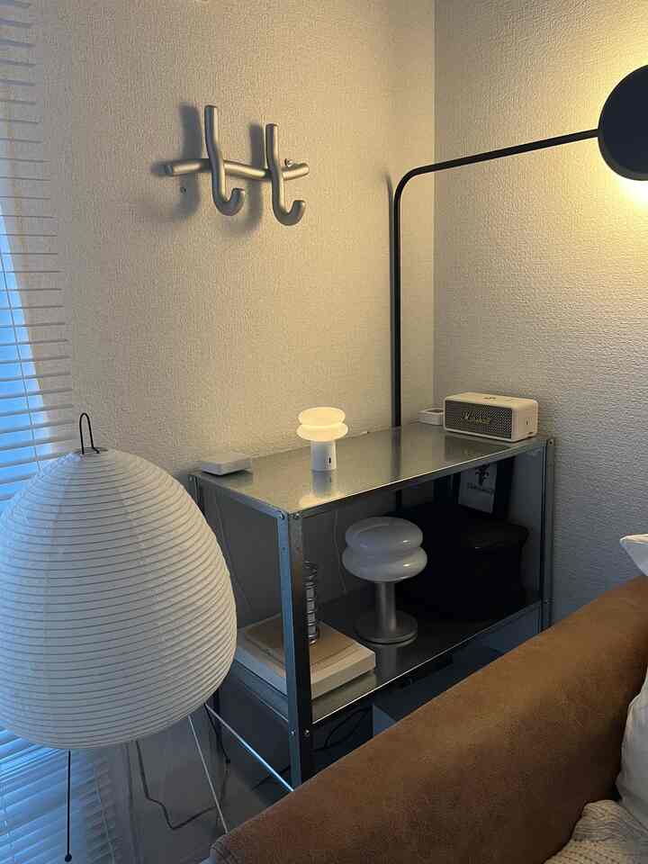 ブラウンのソファとメタルの棚、白いフロアランプが配置されたモダンな1LDKのリビングコーナー