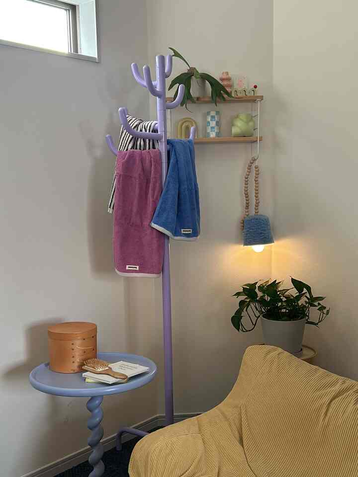 A cozy, simple corner featuring a lavender coat rack and side table, yellow sofa, and green plant