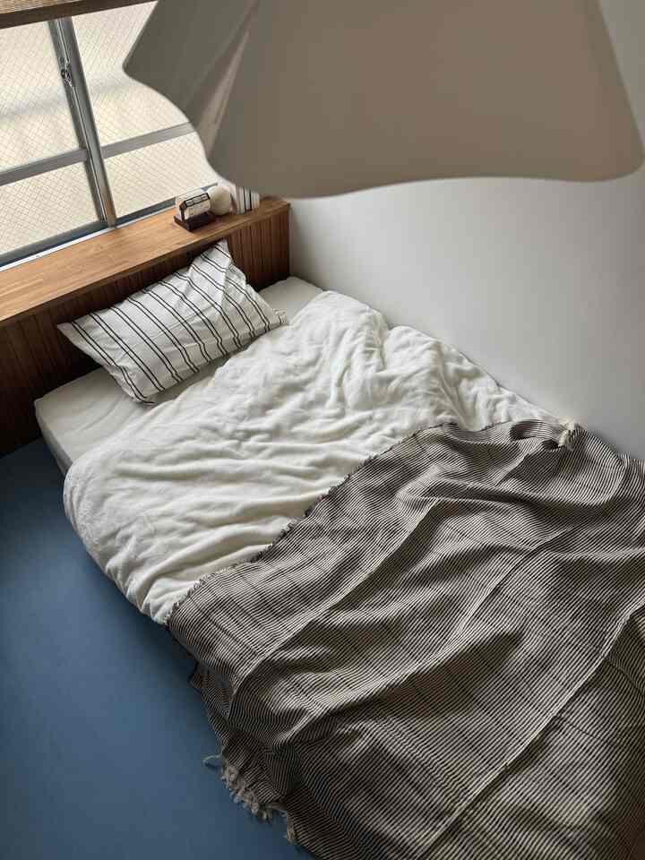 White walled small bedroom featuring a wood tone headboard, a neatly made bed with striped pillow and blanket