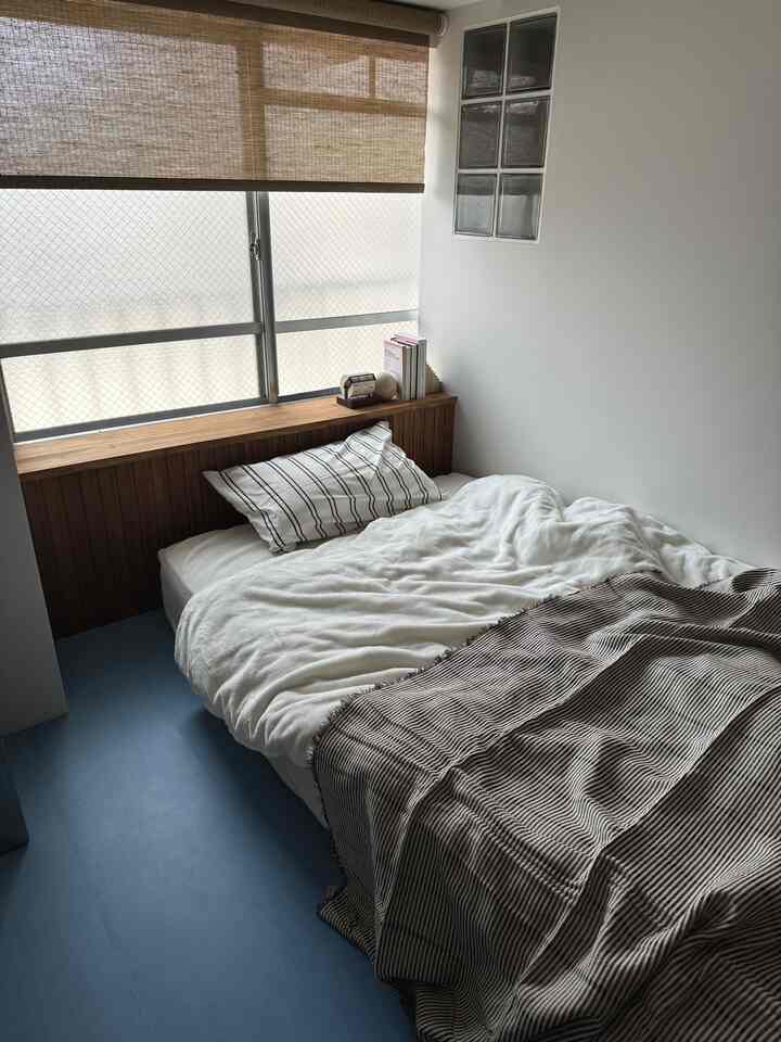 ブラウンとホワイトの落ち着いたトーンの寝室、窓と木製ヘッドボードが配置されたシンプルなインテリア