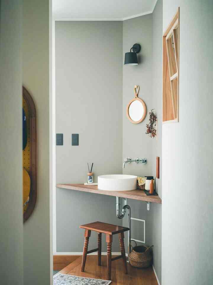 Gray-walled entrance space with wood tone flooring, rattan round mirror, and vintage stool featuring a simple wash basin setup