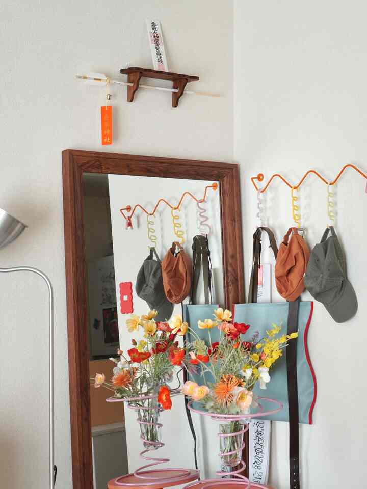 ナチュラルな木目調の鏡とプラントスタンド、鮮やかな花飾りと神棚が配置された玄関のインテリア