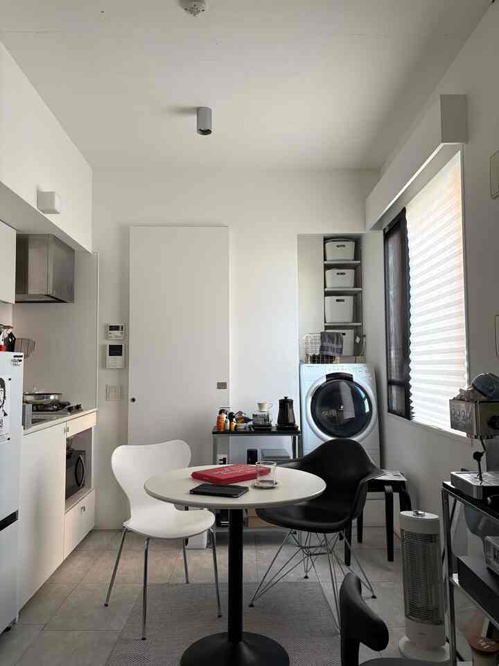Monotone studio kitchen featuring a round dining table, chairs, and an espresso machine in a clean setting