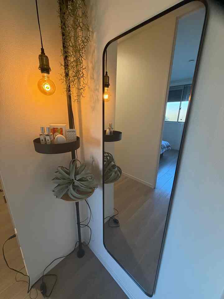 白い壁と茶色の床が調和する狭い玄関、DRAW A LINEの棚と大型IKEA鏡が配置されたモダンなインテリア