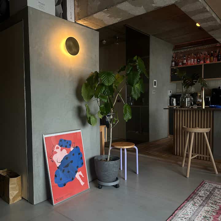 Modern living room and kitchen with natural colors and wood tones, accentuated by large leafy plant and framed poster