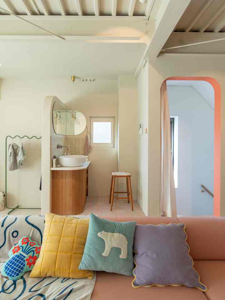 Soft white toned living room with a sofa adorned with yellow and purple cushions, adjacent to a cozy bathroom area