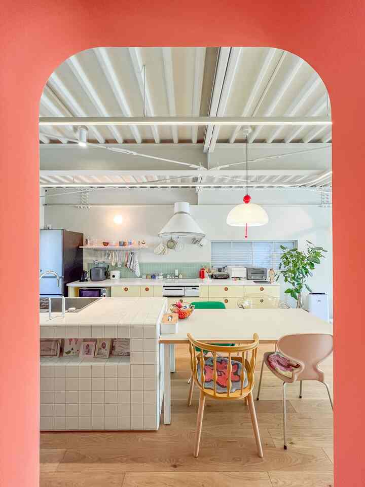 レッドのアーチ入口とナチュラルカラーの床がある、ダイニングテーブルとペンダントライトを配した印象的なオープンキッチン空間