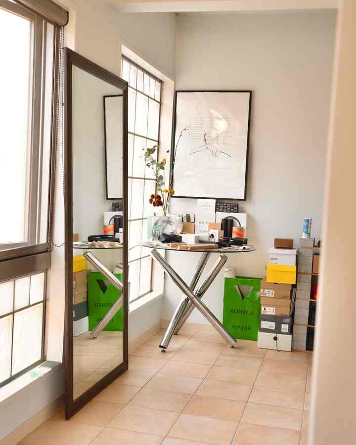White-walled small room with brown tiled floor featuring a round chrome-legged table and large full-length mirror