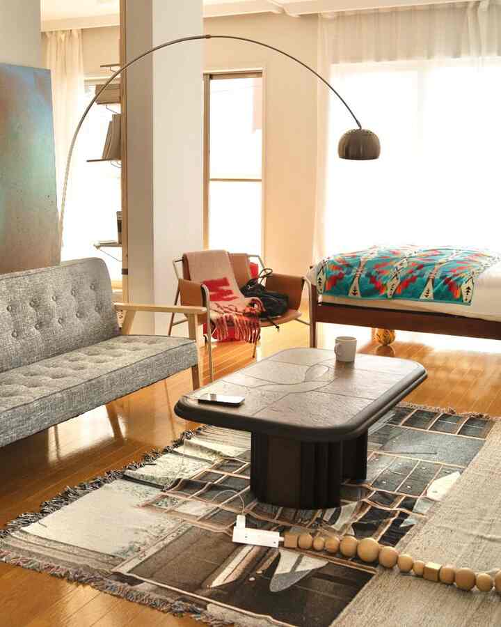 Natural-toned studio apartment living bedroom featuring modern sofa, bed, floor lamp, and coffee table with wood flooring