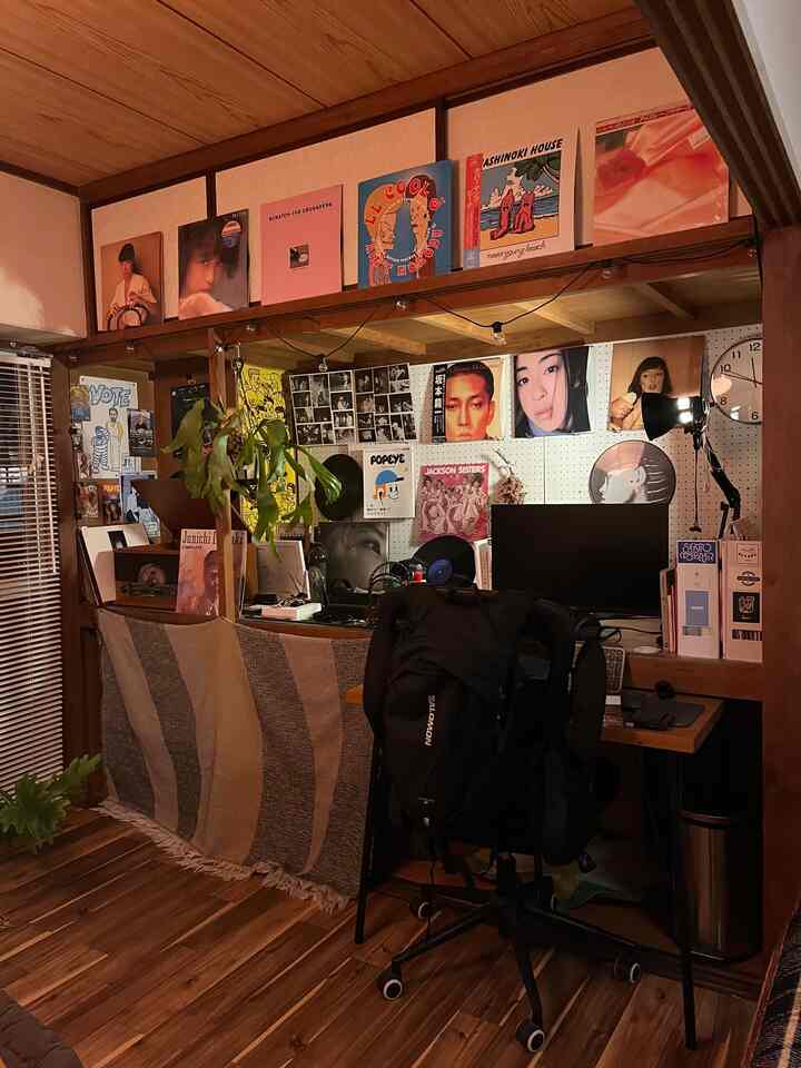 温かみのある木目調のコンパクトなホームオフィス、デスクとチェア、壁面には音楽のポスターと収納アイデアが配置された雰囲気のあるインテリア