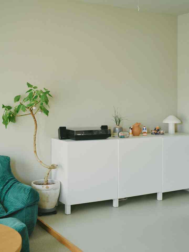 A simple space with white walls, floor, and a BESTÅ storage unit; green sofa and potted plant add accent