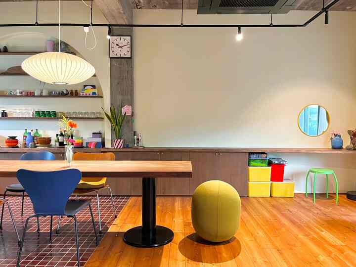 木目調の床が印象的な中規模ダイニングルーム、ペンダントライトとカラフルなダイニングチェアが配されたミッドセンチュリーモダンの空間