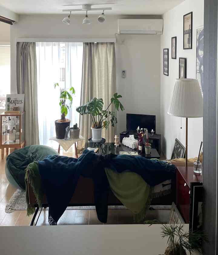 白とベージュを基調にした1LDKリビング、ソファと棚、植物、フロアランプが配置されたナチュラルで落ち着いた雰囲気のインテリア