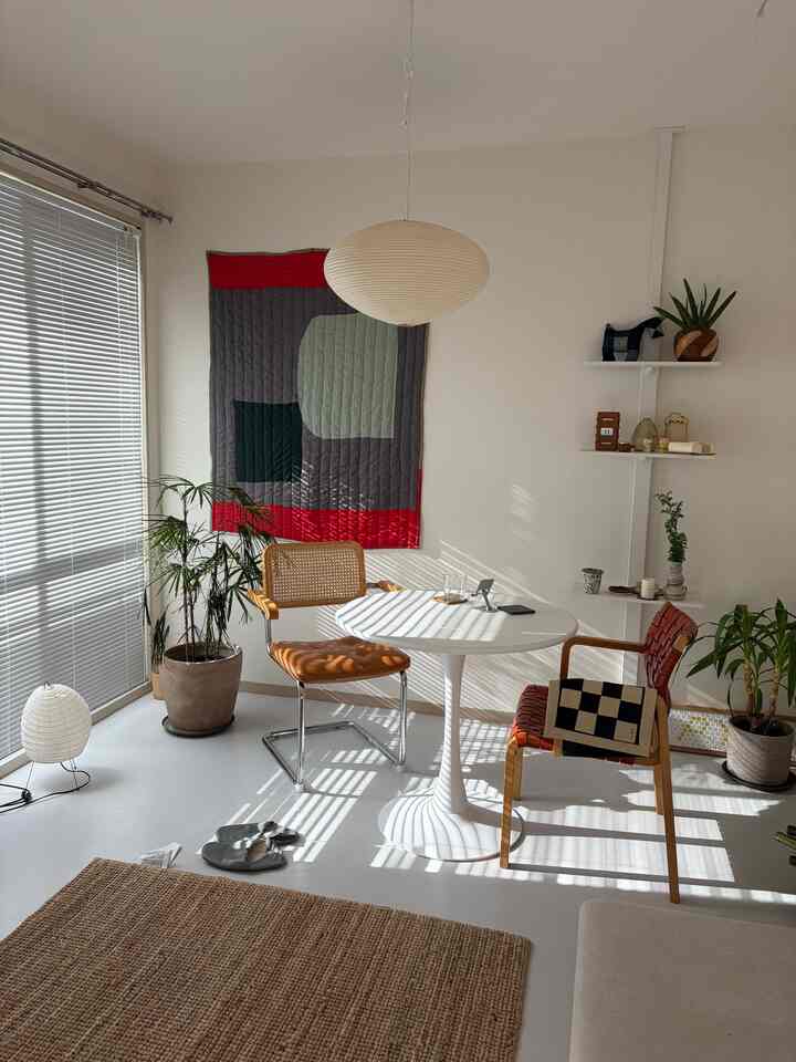 白い壁と床、丸いダイニングテーブル、茶色い椅子、自然素材のラグ、植物が配置されたナチュラルモダンなダイニングルーム