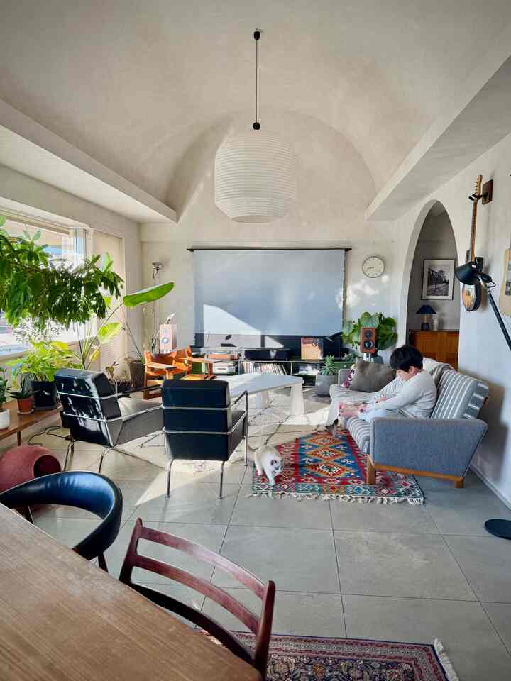 明るいアイボリー色のリビング、ミッドセンチュリーモダンのソファと椅子が配置されたヴィンテージの雰囲気あるインテリア、ラグの上に猫がいる