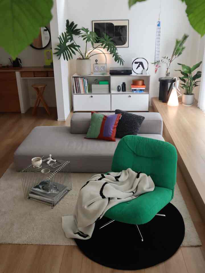 Modern living room with white walls and wood flooring, featuring a green armchair and a gray sofa in a natural style