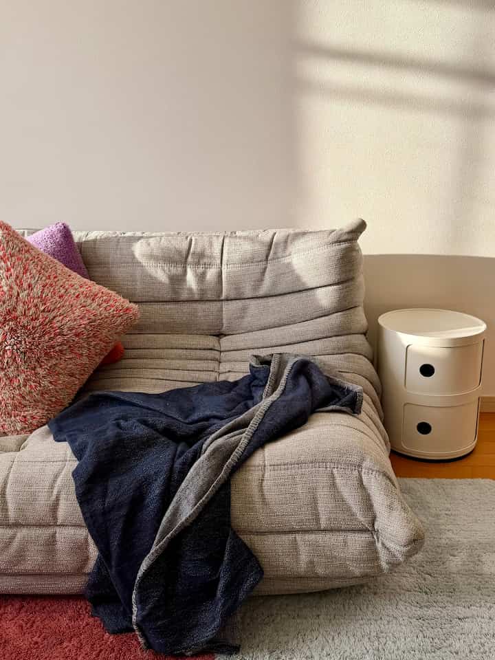 暖かいベージュ色調のリビング、広々としたソファと白いサイドテーブル、心地良いブランケットとクッションが配置された雰囲気のあるインテリア