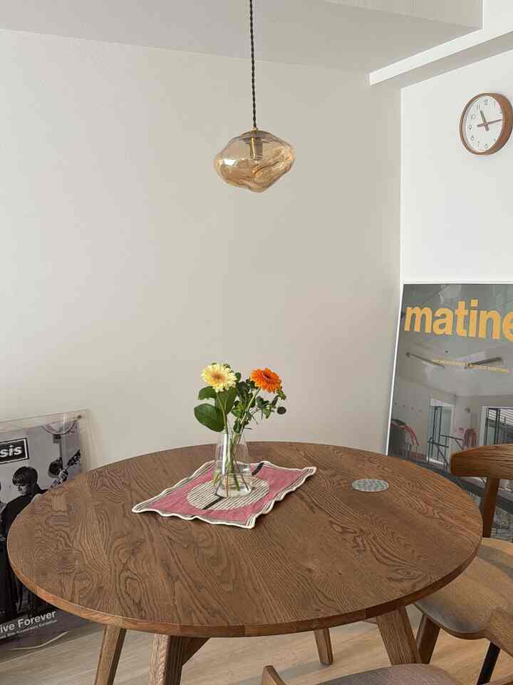 白い壁と木目調の丸いダイニングテーブルが配置されたシンプルモダンなダイニング、ペンダントライトが温かみのある雰囲気を演出