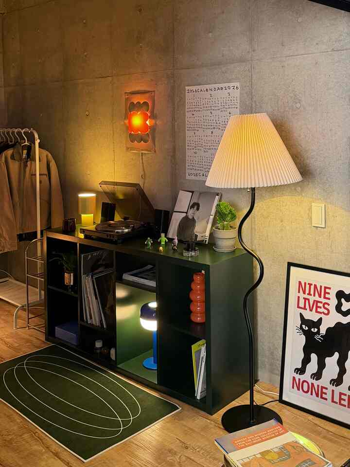 ナチュラルな木目調の床とグレーのコンクリート壁があるモダンなリビング、コンソールテーブルや多様な照明、小さな植物が配置された空間