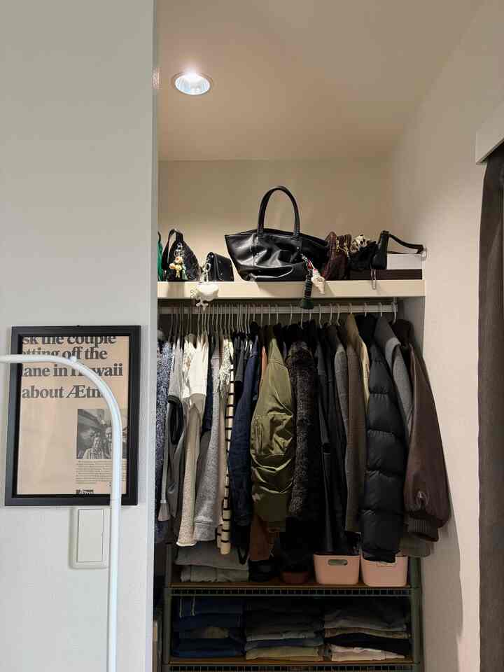 白い壁と天井の1LDKクローゼット、中央に掛けられたさまざまな色の服と上部の棚に整頓されたバッグが配置された印象的な収納空間