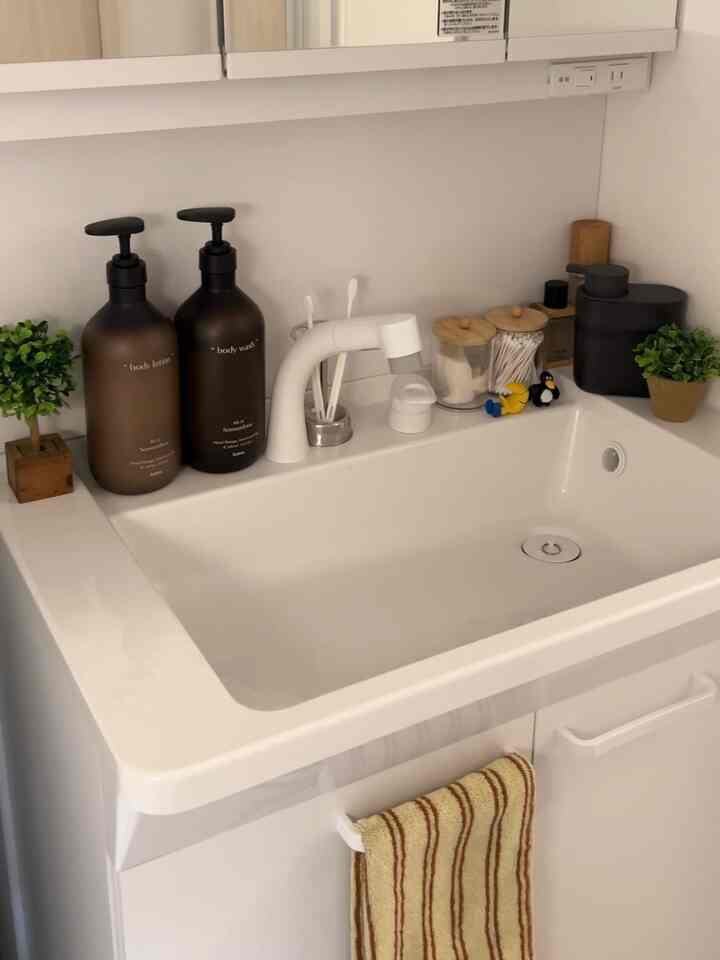 ホワイトトーンの洗面台、ミニマルで清潔感のあるデザインに多様な小物が配置された印象的な空間