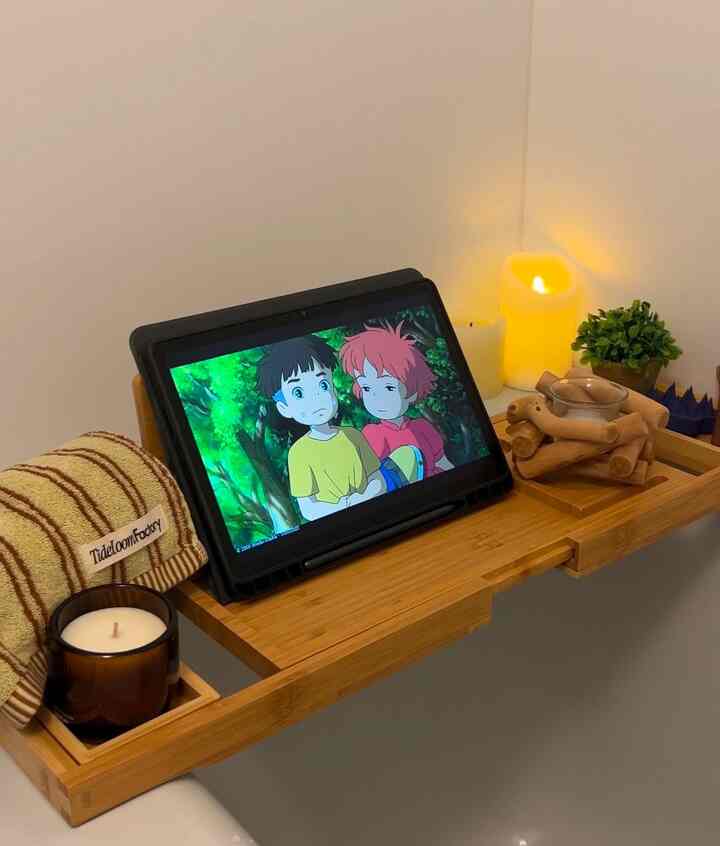 ナチュラルなウッドトーンのバスルーム、浴槽の上に配置されたキャンドルやタオルとデジタルタブレットが落ち着いた雰囲気を醸し出すインテリア