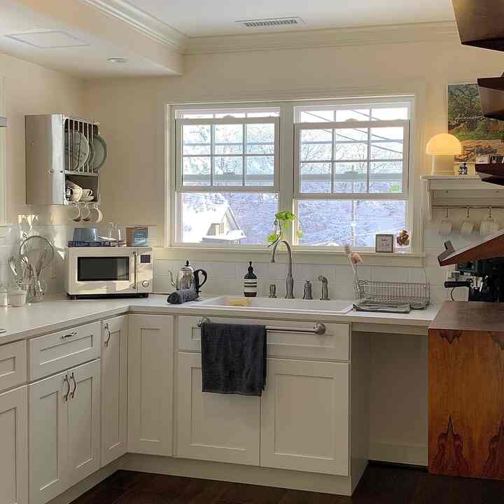 明るい白を基調としたキッチン空間、大きな窓と食器棚、ネイビーのキッチンタオルが配置された清潔感あるナチュラルモダンなインテリア