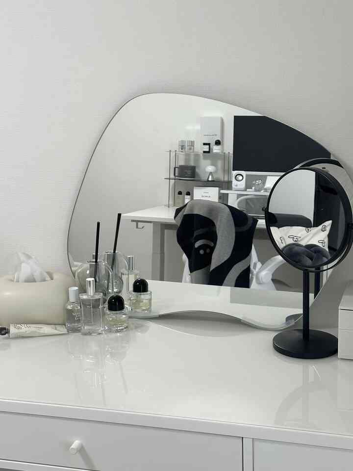 Simple white-toned space featuring a uniquely shaped wall mirror and a vanity desk with organized items
