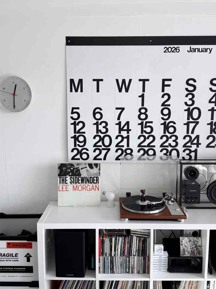 ホワイトトーンのリビング、モダンでミニマルな棚にレコードプレーヤーと音楽関連のアイテムが配置された印象的な空間