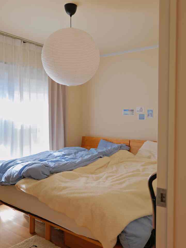 A 6-tatami bedroom with beige walls and wooden bed, featuring blue duvet cover and white curtains for a bright, natural atmosphere