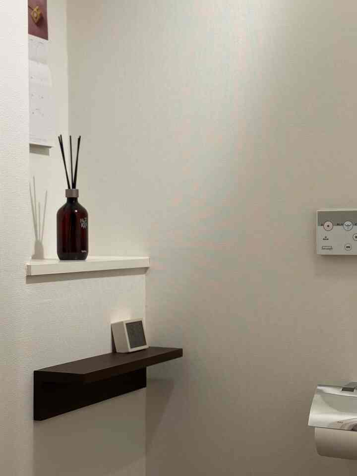 白いトーンの小さなトイレにディフューザーと2つの棚が配置されたミニマルで清潔感のあるインテリア