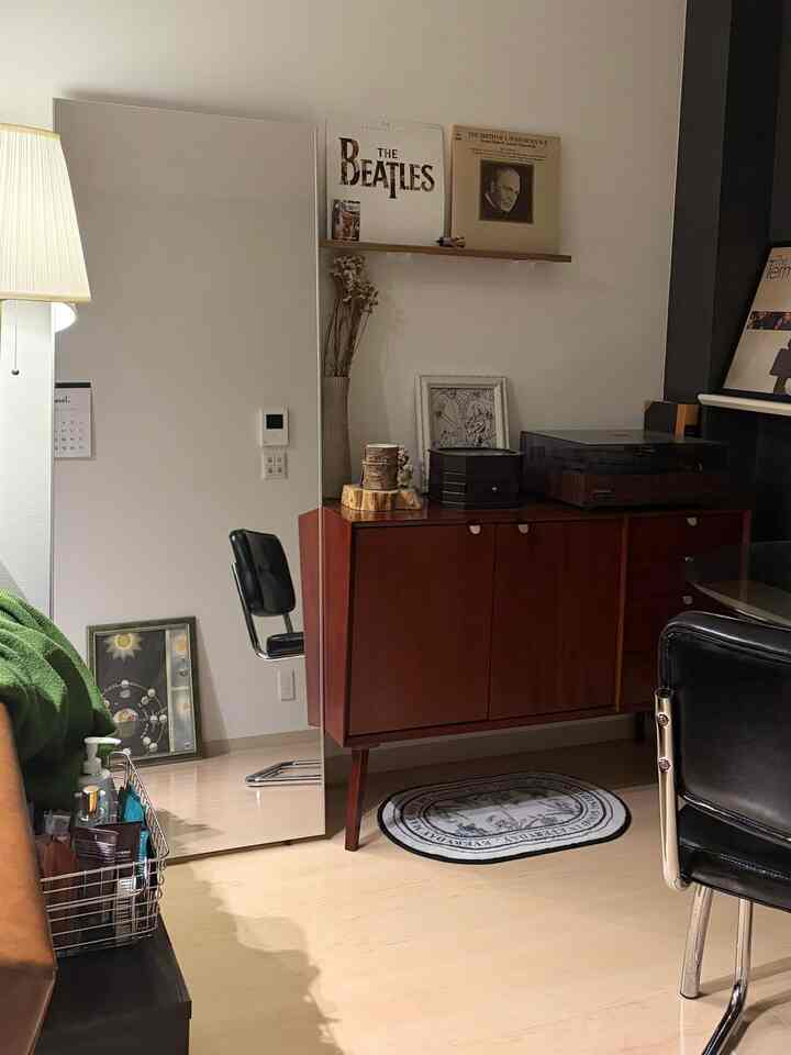 白い壁と木目調のキャビネットが配置されたモダンなリビング、全身鏡とヴィンテージ風の小物が置かれた落ち着いたインテリア