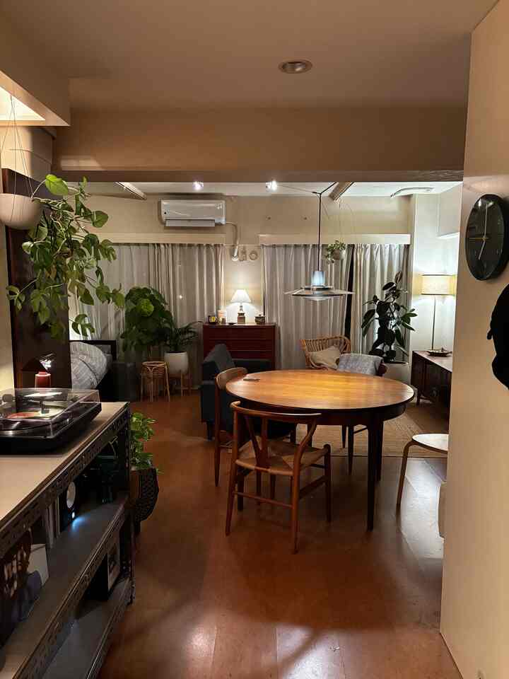 温かみのあるブラウンと木目調のヴィンテージリビング、丸いダイニングテーブルとペンダントライト、植物が配置された雰囲気のある空間