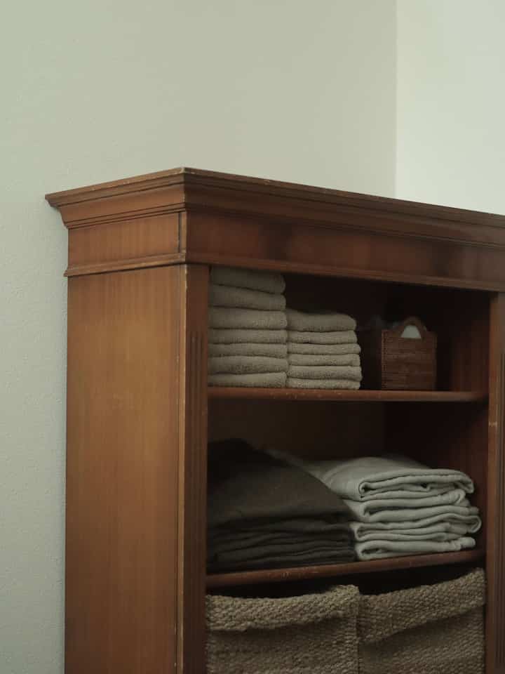 ナチュラルな色調の脱衣所、ヴィンテージの木製棚にタオルとラタンのバスケットが整然と配置された雰囲気のあるインテリア