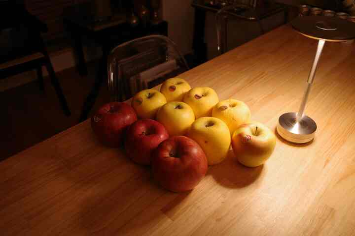 温かみのあるオレンジ色の木製ダイニングテーブルに並んだ赤と黄色のりんごが印象的なナチュラルな1LDKのリビング空間