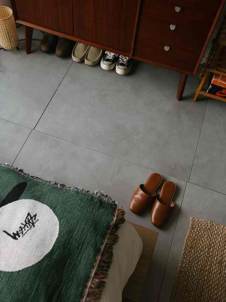 グレーのタイル床とブラウンの靴箱が配置された玄関スペース、緑色のラグとブラウンのスリッパが見えるすっきりとした室内