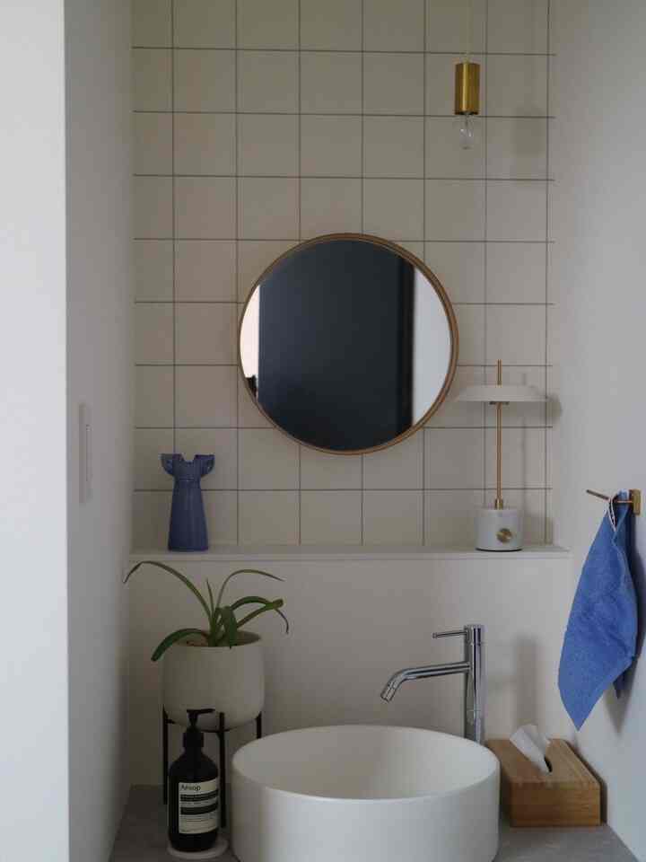 White, blue, and gold toned bathroom featuring a round mirror and table lamp with simple, natural interior design