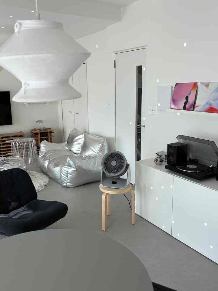 白とシルバーのトーンのリビング、ビーズクッションソファとアームチェアが配置された印象的でやや散らかった空間