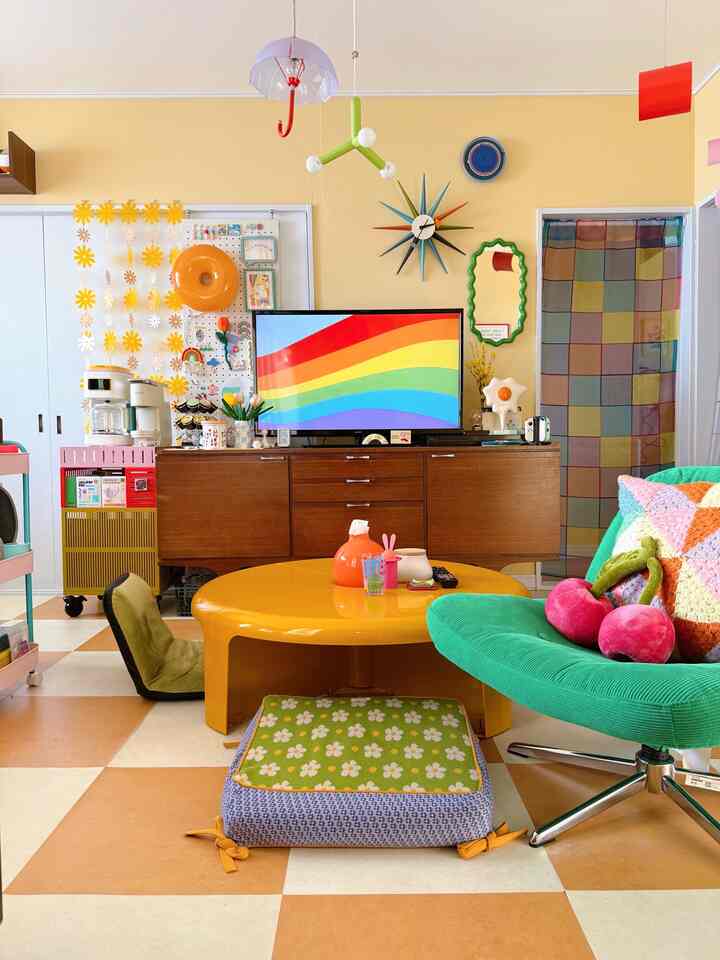 黄色い壁とカラフルなチェック柄のカーテン、緑のアームチェアと黄色の丸いテーブルが配置されたレトロなリビングルーム