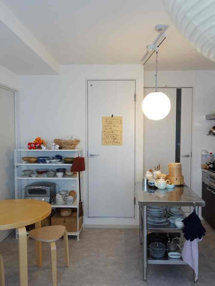 A white and light gray toned kitchen featuring a stainless steel worktable and Muji shelving unit creating a clean storage space