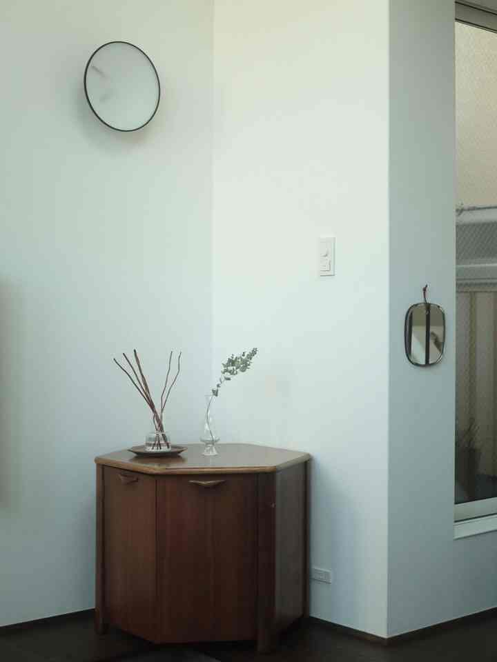 Bright-toned walls and dark flooring corner with a brown wooden console holding glass vases, simple natural modern space