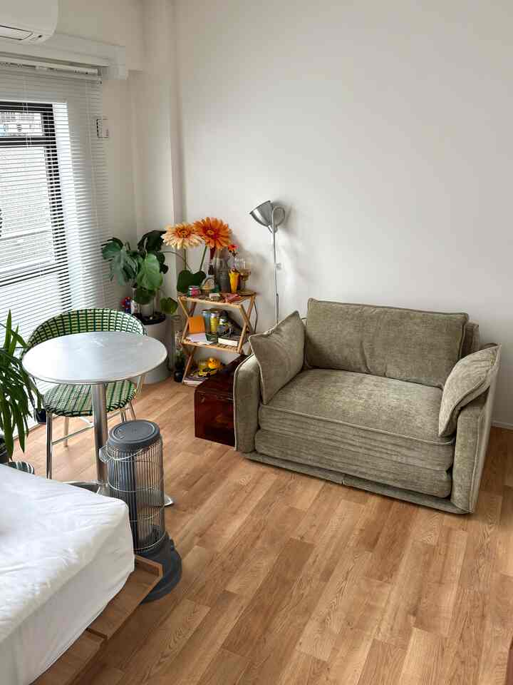 ナチュラルカラーのワンルームリビング、オリーブグリーンのソファとアルミニウムのラウンドテーブルが置かれた雰囲気のあるインテリア