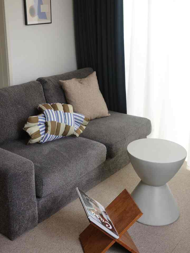 Natural-toned living room with a gray sofa, navy curtains, wooden book stand, and gray side table